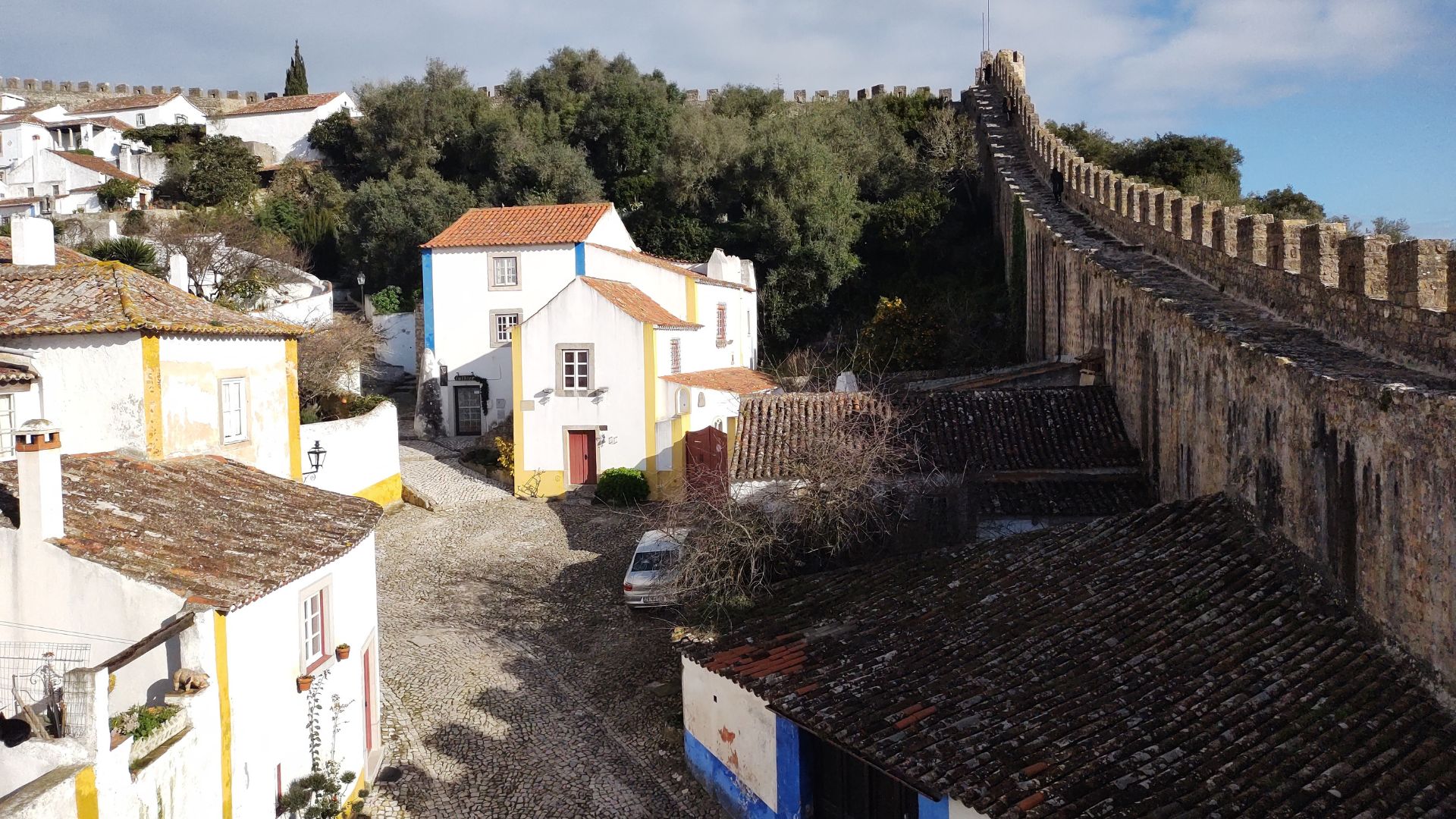A view of the historic town of Óbidos, Portugal, featuring its medieval walls, cobblestone streets, and white-washed houses with terracotta roofs.