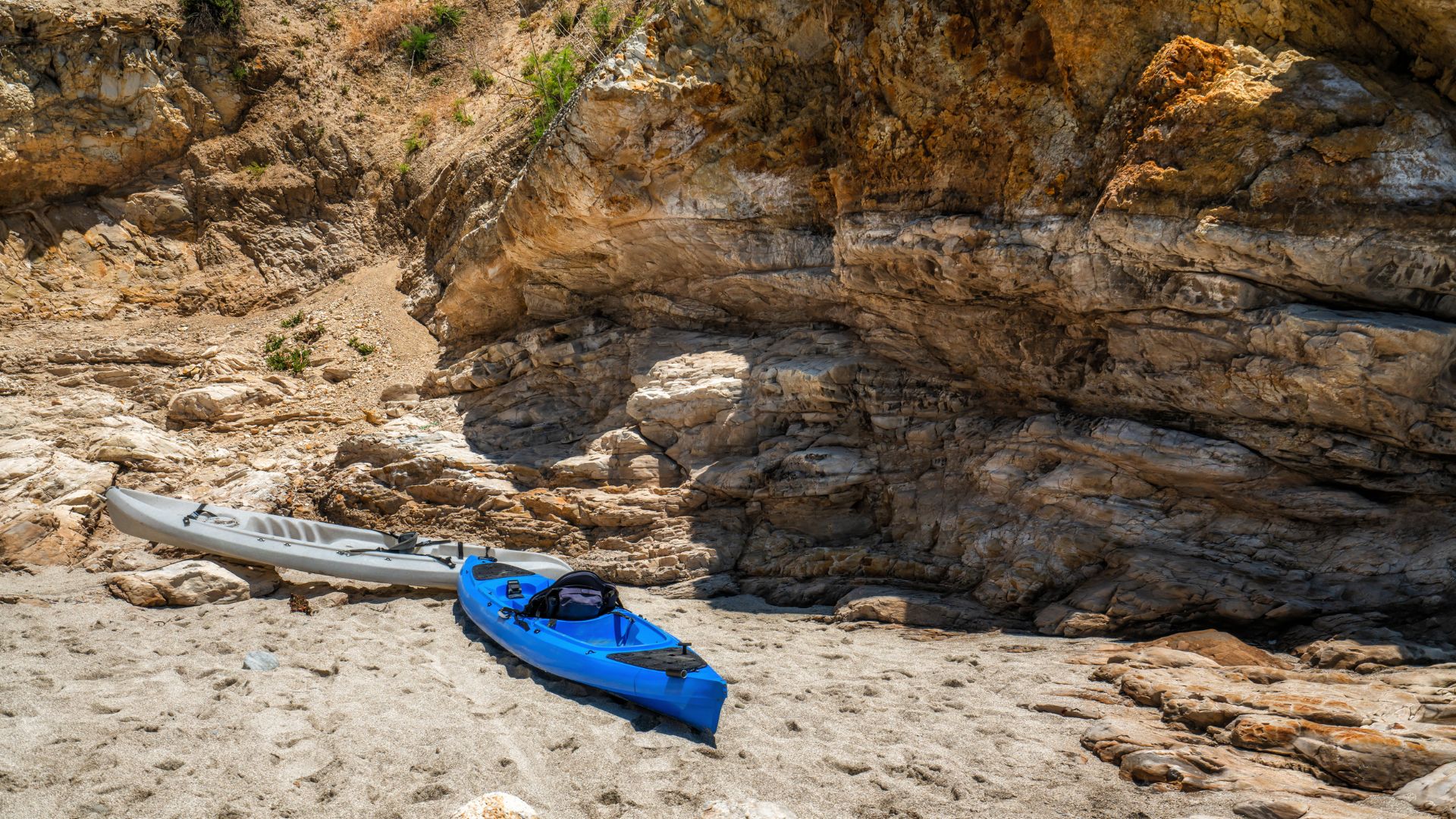 The image shows a sandy beach with large rock formations and kayaks.