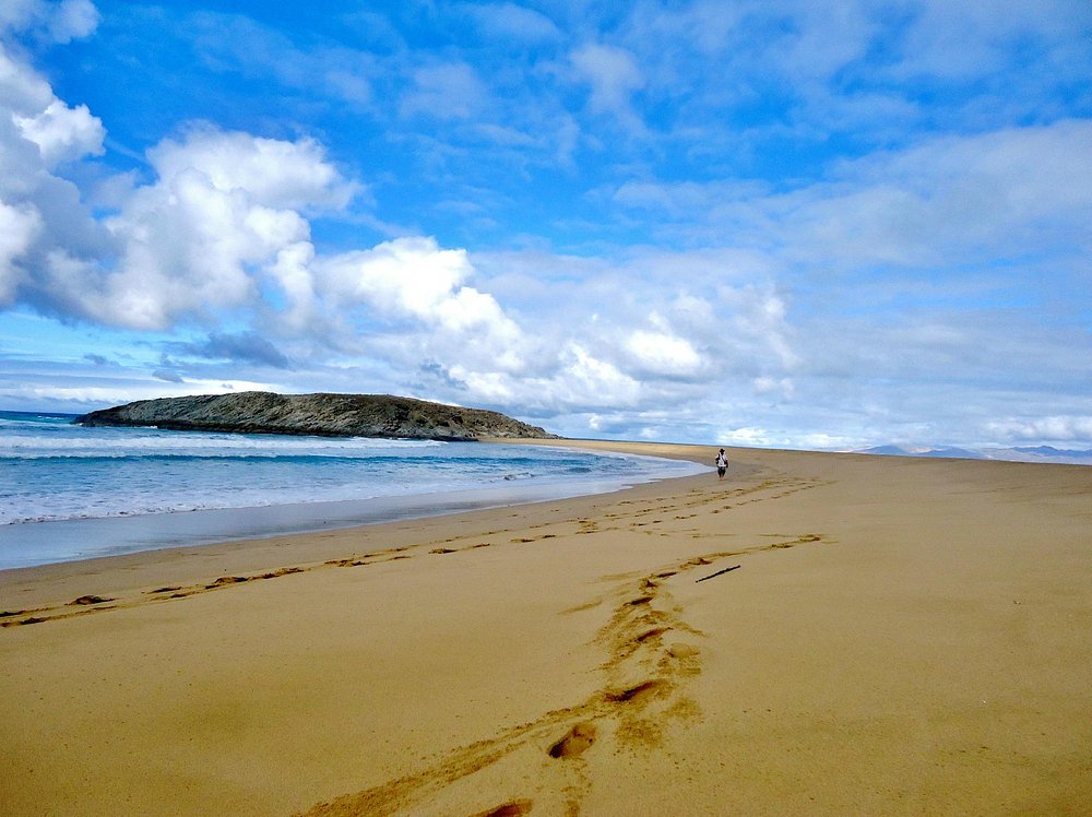 A lone person walking along the windswept shore of Cofete Beach