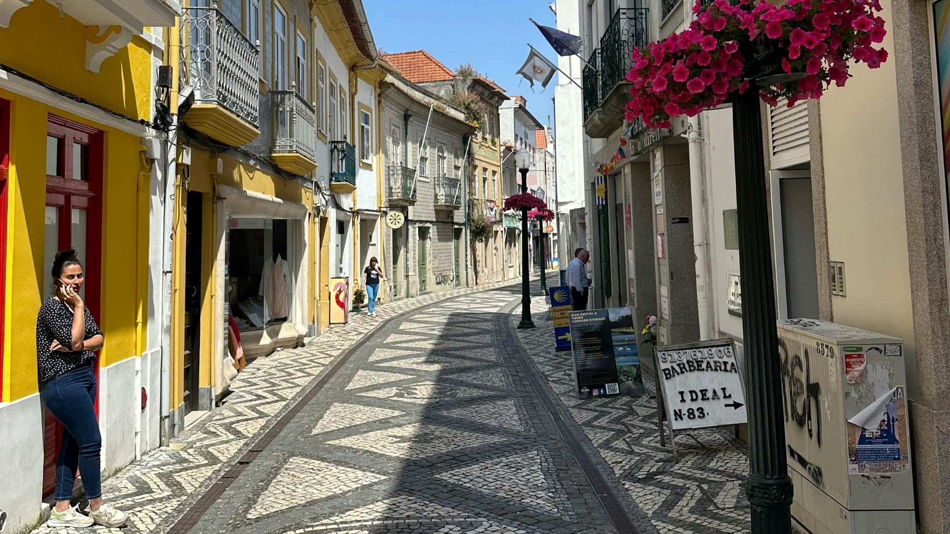 A charming, narrow cobblestone street in Coimbra, Portugal, with traditional buildings featuring colorful facades and intricate mosaic patterns on the pavement.