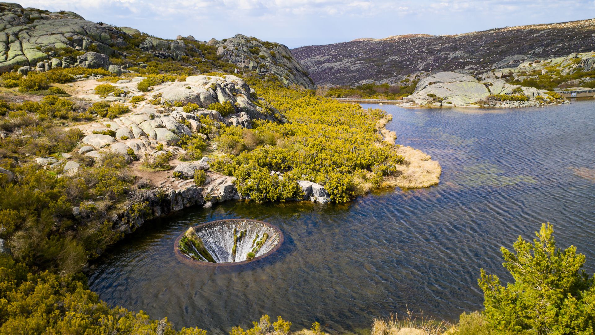 Covão dos Conchos is known for its unique bell-mouth spillway, which creates a striking visual effect resembling a "hole" in the middle of the lake. 