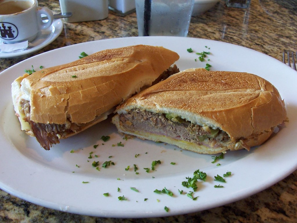 Close-up of a traditional Cuban sandwich with roast pork, ham, Swiss cheese, pickles, and mustard on pressed Cuban bread.