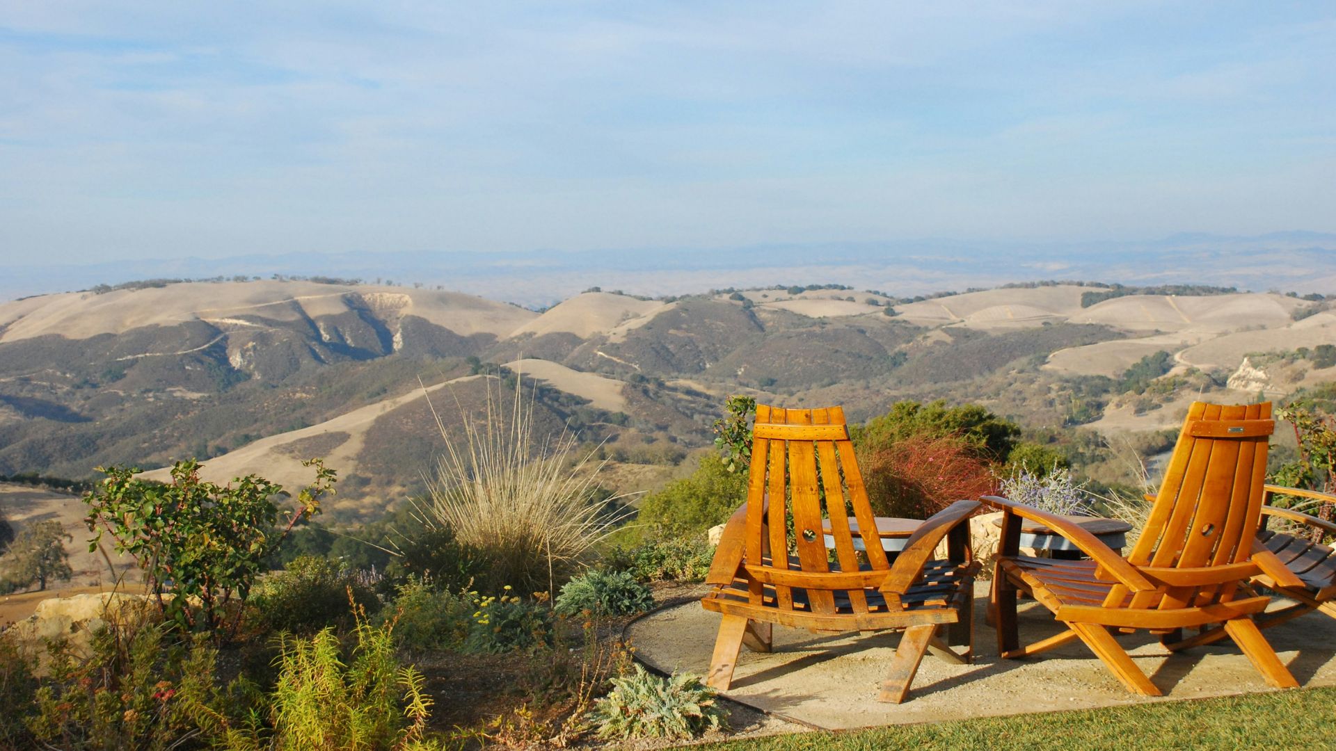 Two wooden Adirondack chairs face a panoramic view of rolling hills and vineyards under a blue sky at DAOU Vineyards in Paso Robles, California.