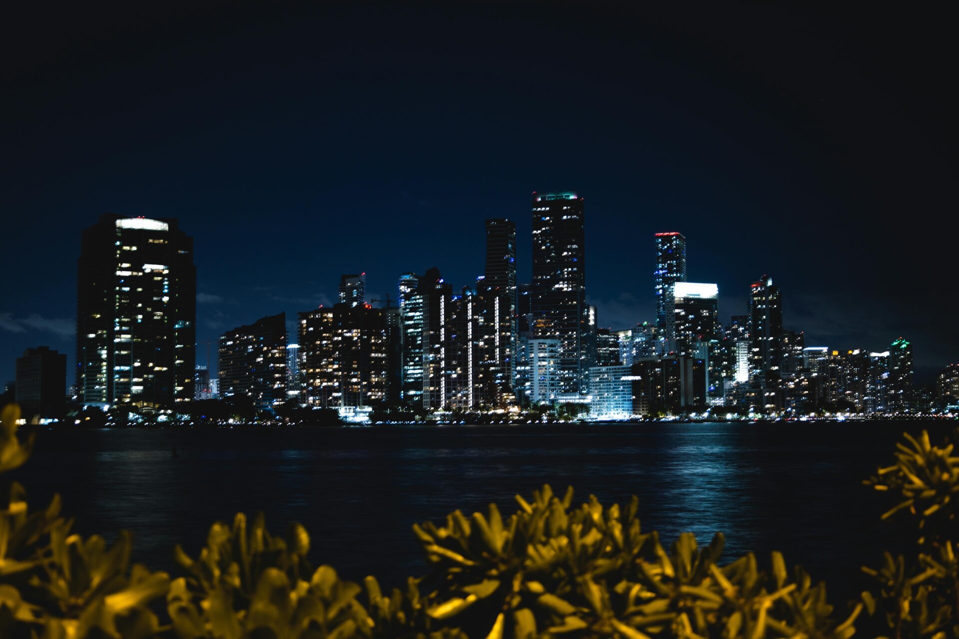 Miami skyline at night with illuminated towers and vibrant reflections shimmering on Biscayne Bay.
