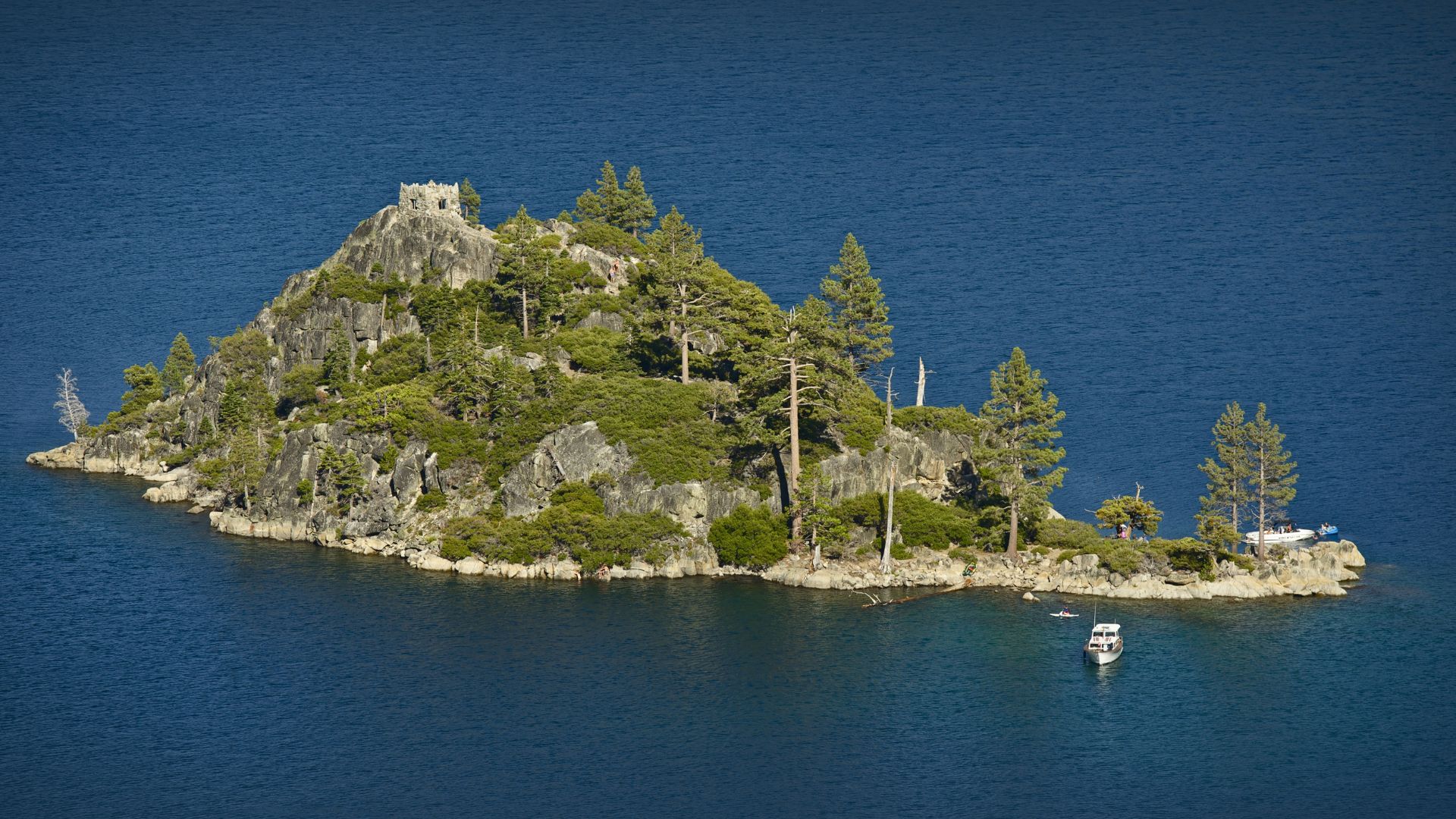 A small, rocky island covered in trees and featuring a stone structure at its summit, surrounded by the deep blue water of Lake Tahoe.