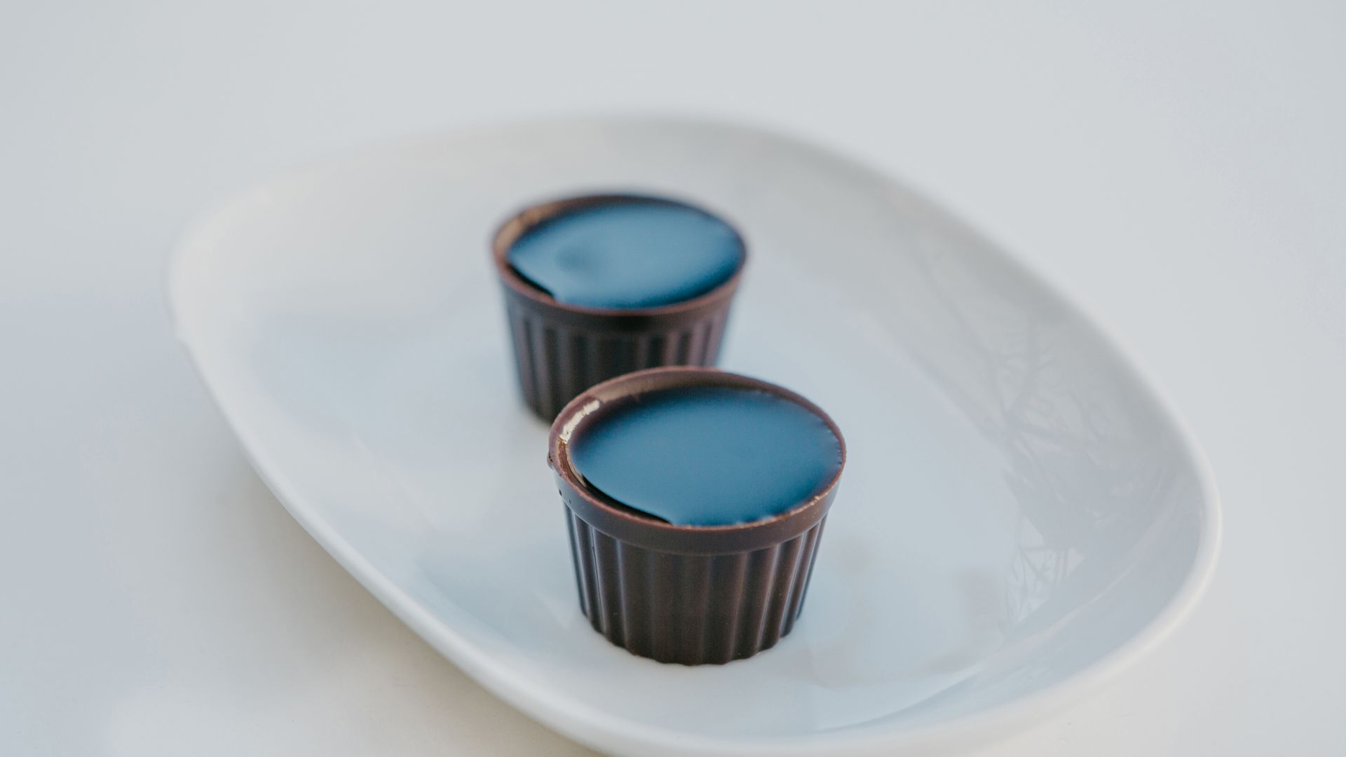 Two chocolate cups filled with a dark liquid, likely Ginjinha liqueur, resting on a white platter.