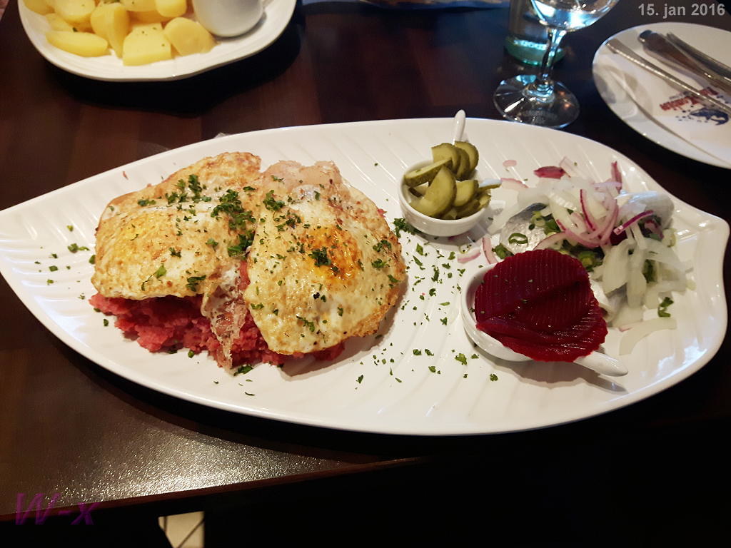 Northern German specialty Labskaus served with fried egg and garnished with pickled vegetables.