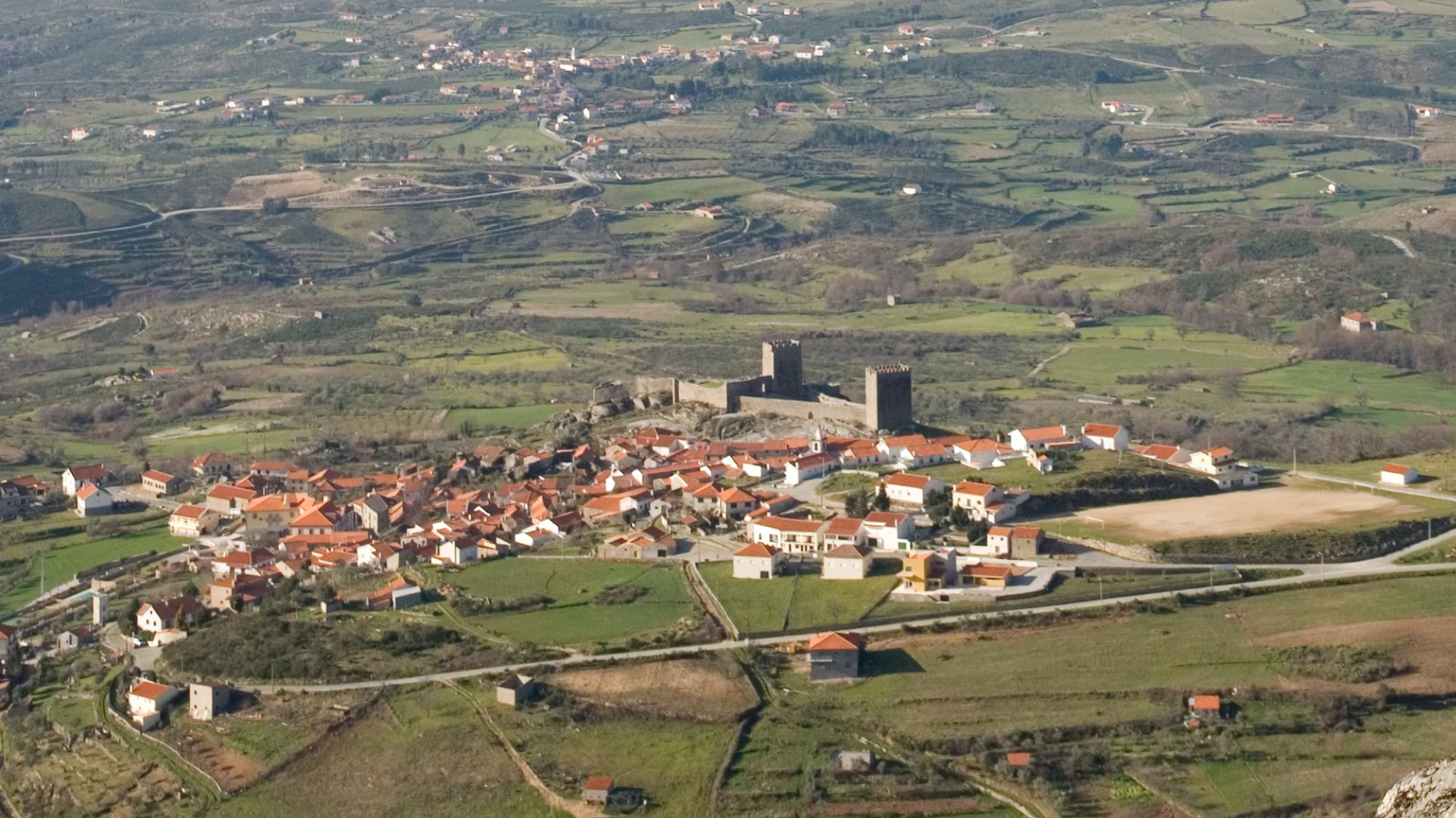 The image captures an aerial view of Linhares da Beira, a picturesque medieval village in Central Portugal, renowned for its well-preserved 12th-century castle, Castelo de Linhares da Beira, which dominates the landscape.