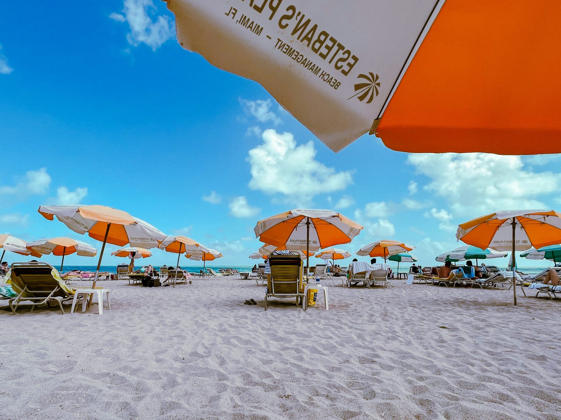 Sunny day at Miami Beach with clear blue skies, white sand, and colorful umbrellas lining the shore.