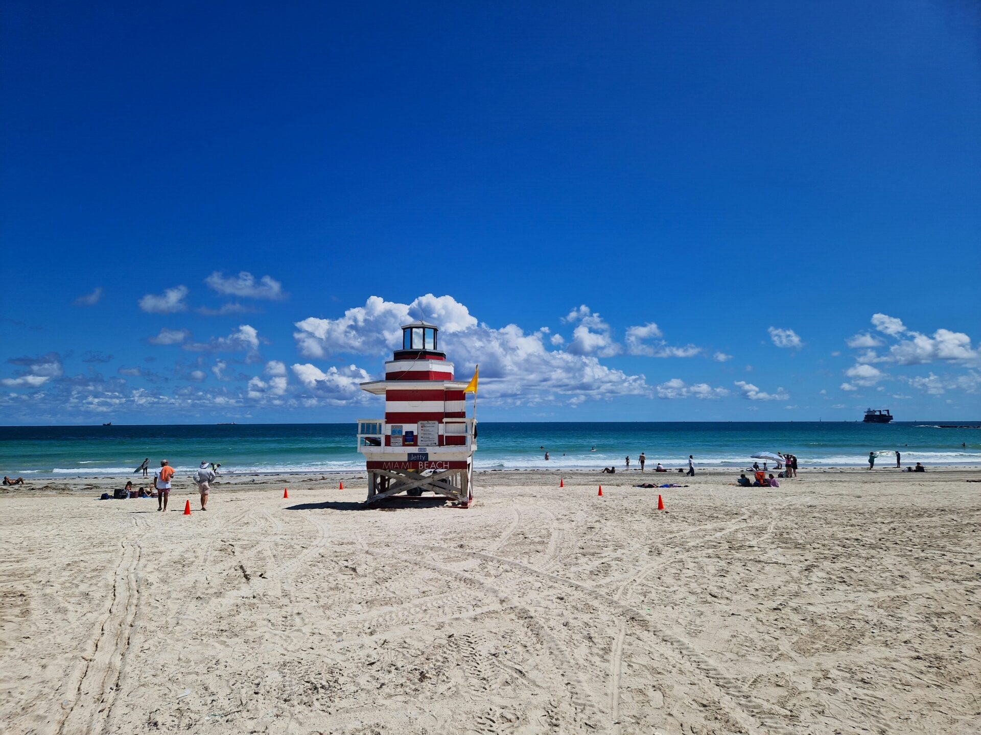 Miami Beach in summer with turquoise ocean waves, beachgoers, and lifeguard towers.

