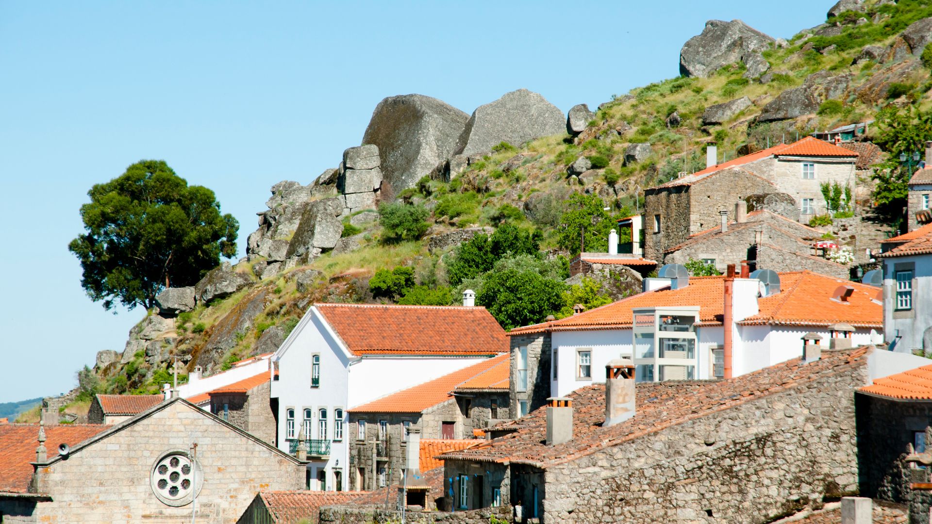 This image captures the unique village of Monsanto, Portugal, renowned for its houses built ingeniously amidst and under giant granite boulders, showcasing a remarkable integration of architecture with the natural landscape. 