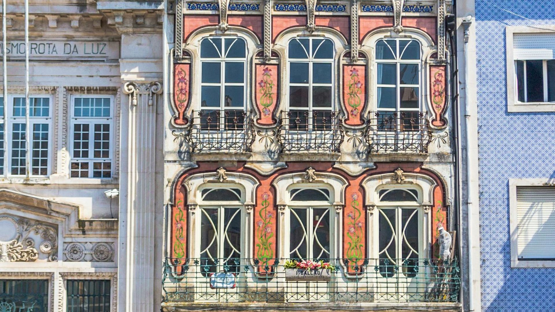 An ornate Art Nouveau building with a white facade, red-framed windows, and decorative balconies stands under a clear blue sky in Aveiro, Portugal.