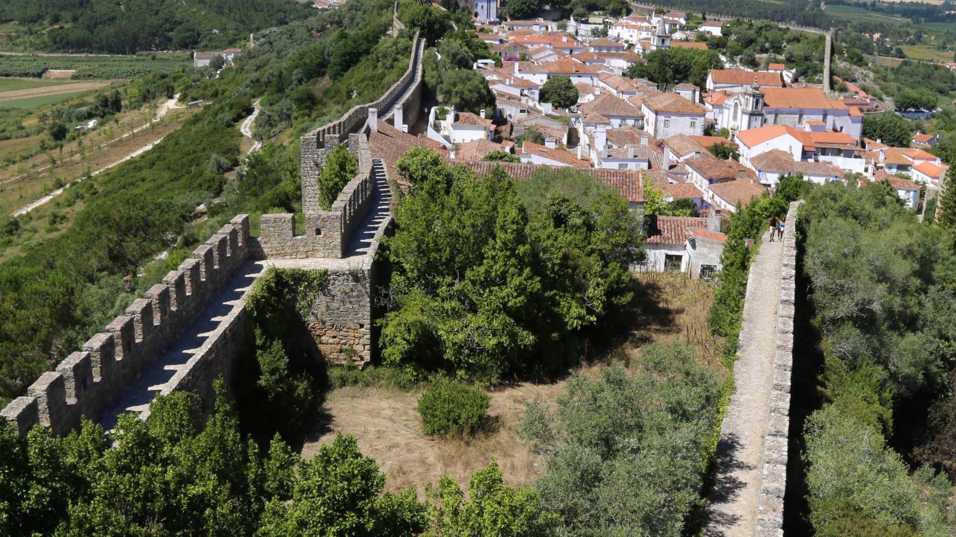 A panoramic view of the medieval walled town of Óbidos, Portugal, with  terracotta-roofed houses nestled on a hillside.