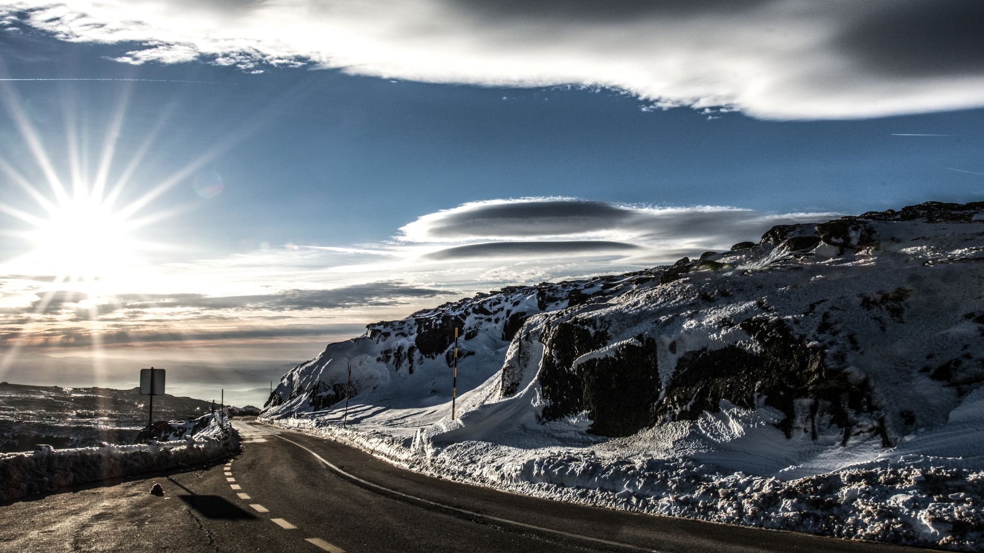 A serene winter landscape showcasing the majestic, snow-capped peaks of Serra da Estrela in Portugal, with a vast mountain range extending into the hazy distance under a clear blue sky and a road.