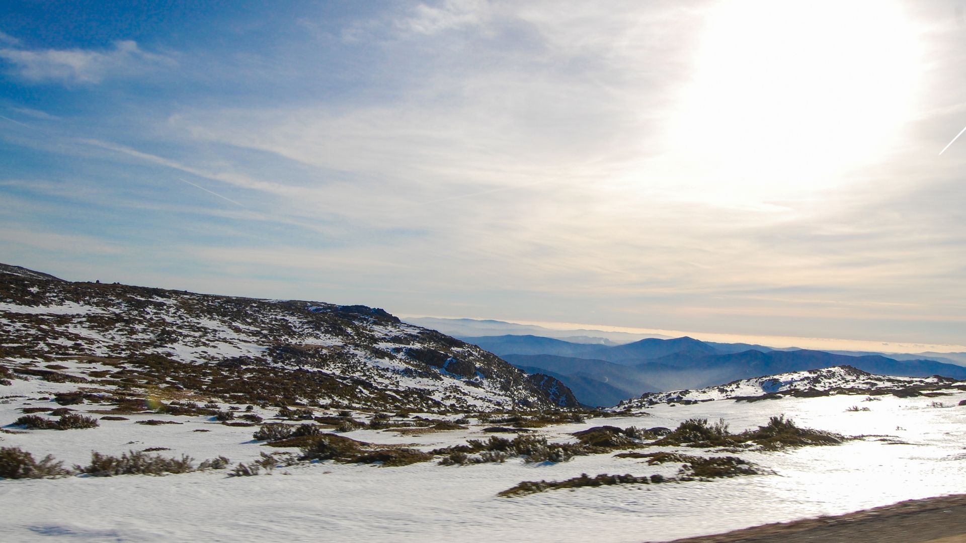A serene winter landscape showcasing the majestic, snow-capped peaks of Serra da Estrela in Portugal, with a vast mountain range extending into the hazy distance under a clear blue sky. 