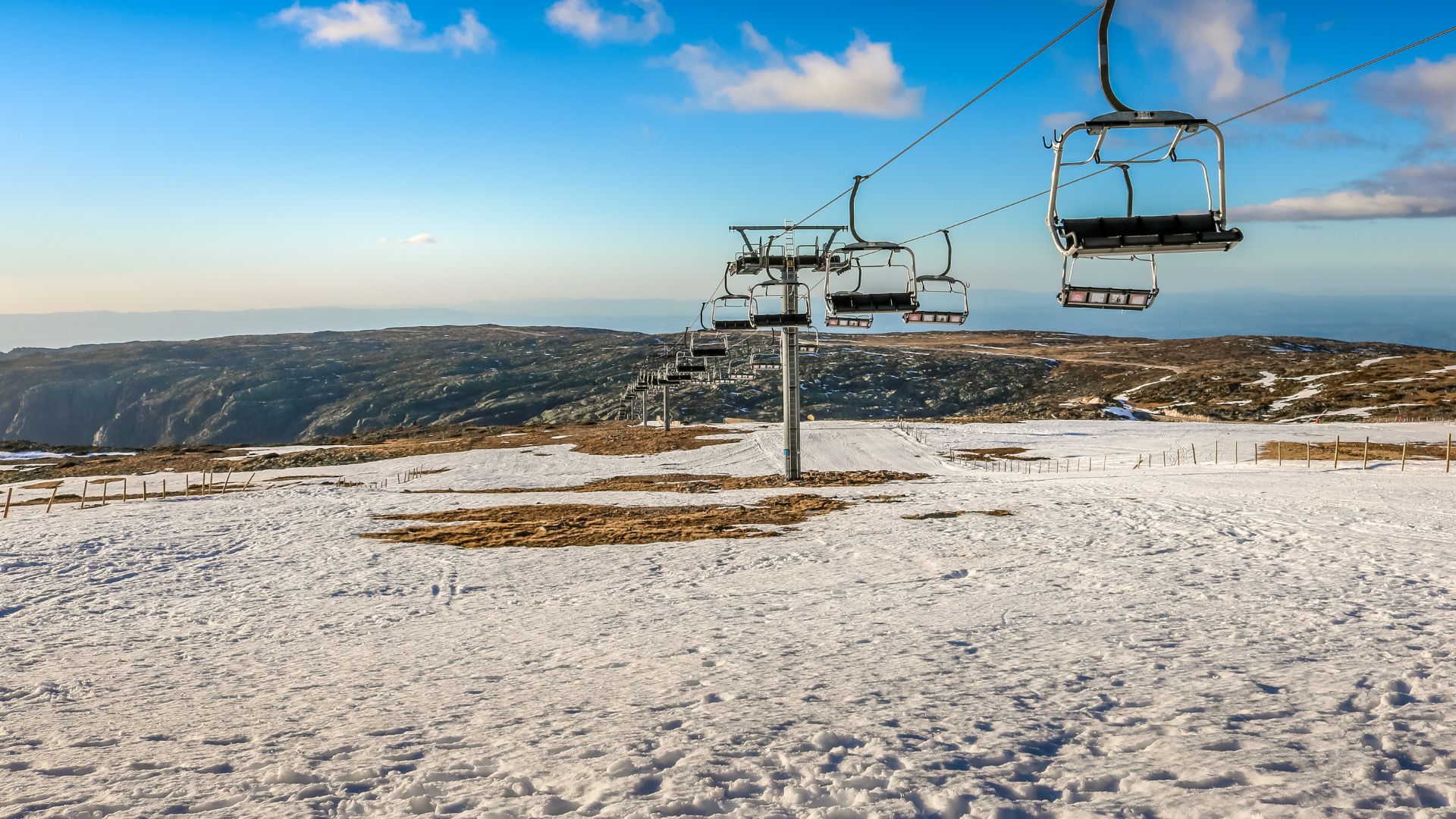 A serene winter scene at the Serra da Estrela ski resort in Central Portugal, featuring snow-covered slopes and ski lifts under a clear sky. 