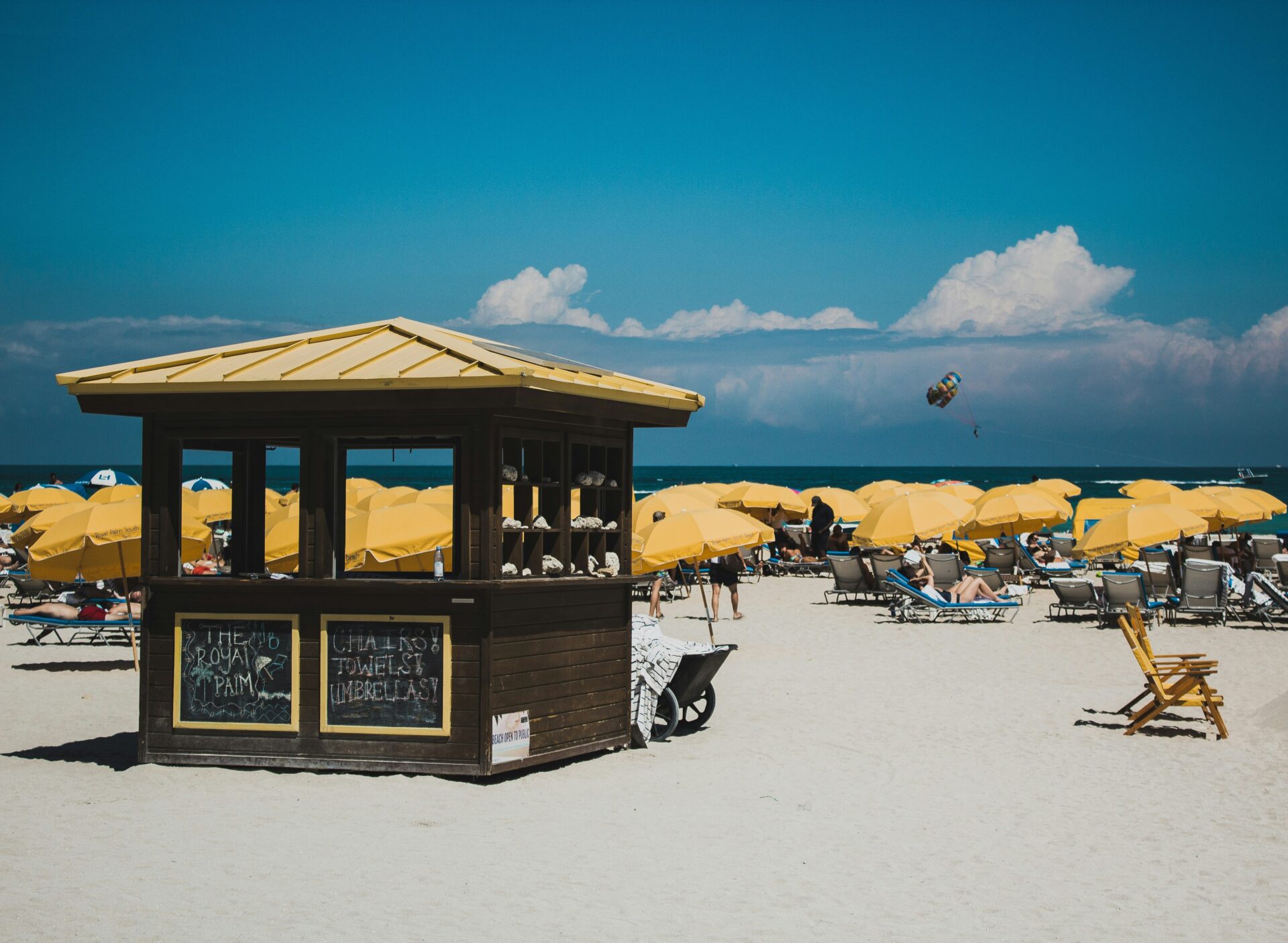 A lively Miami Beach scene with a crowd of sunbathers lounging under colorful umbrellas on the golden sand.