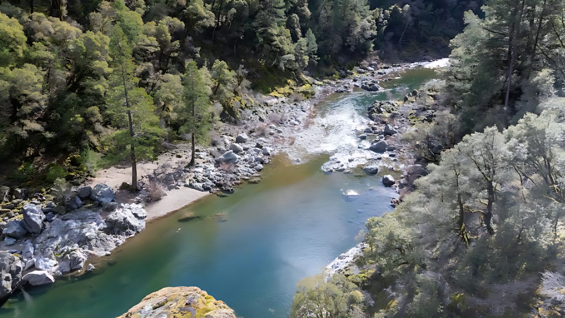An aerial view captures the vibrant turquoise waters of the South Yuba River winding through a verdant, rocky canyon in California, flanked by lush green forests on both sides.