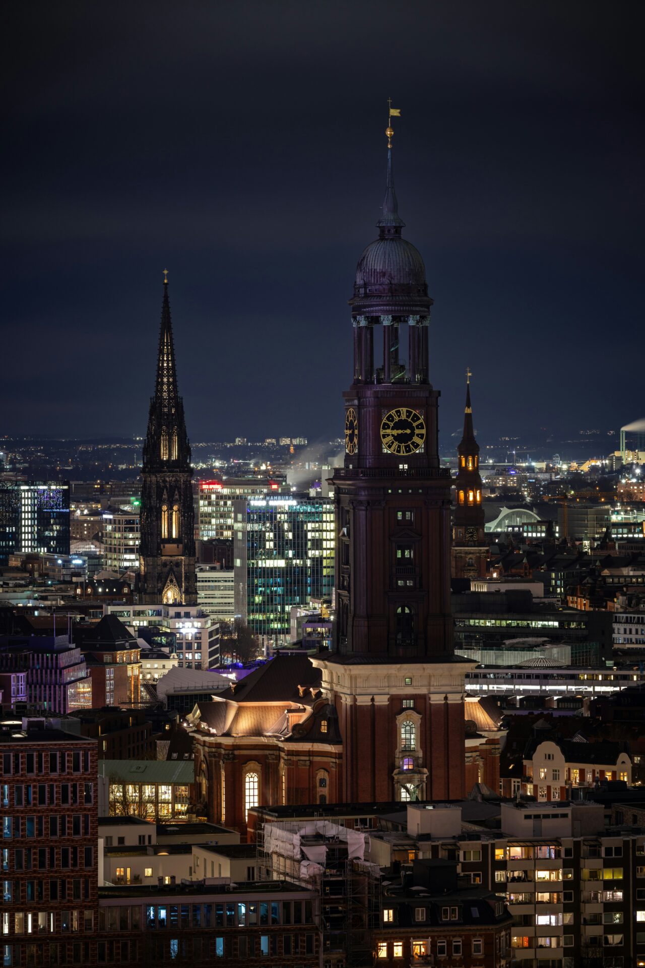 St. Michael's Church at night, its illuminated spire rising dramatically against the darkened Hamburg skyline.