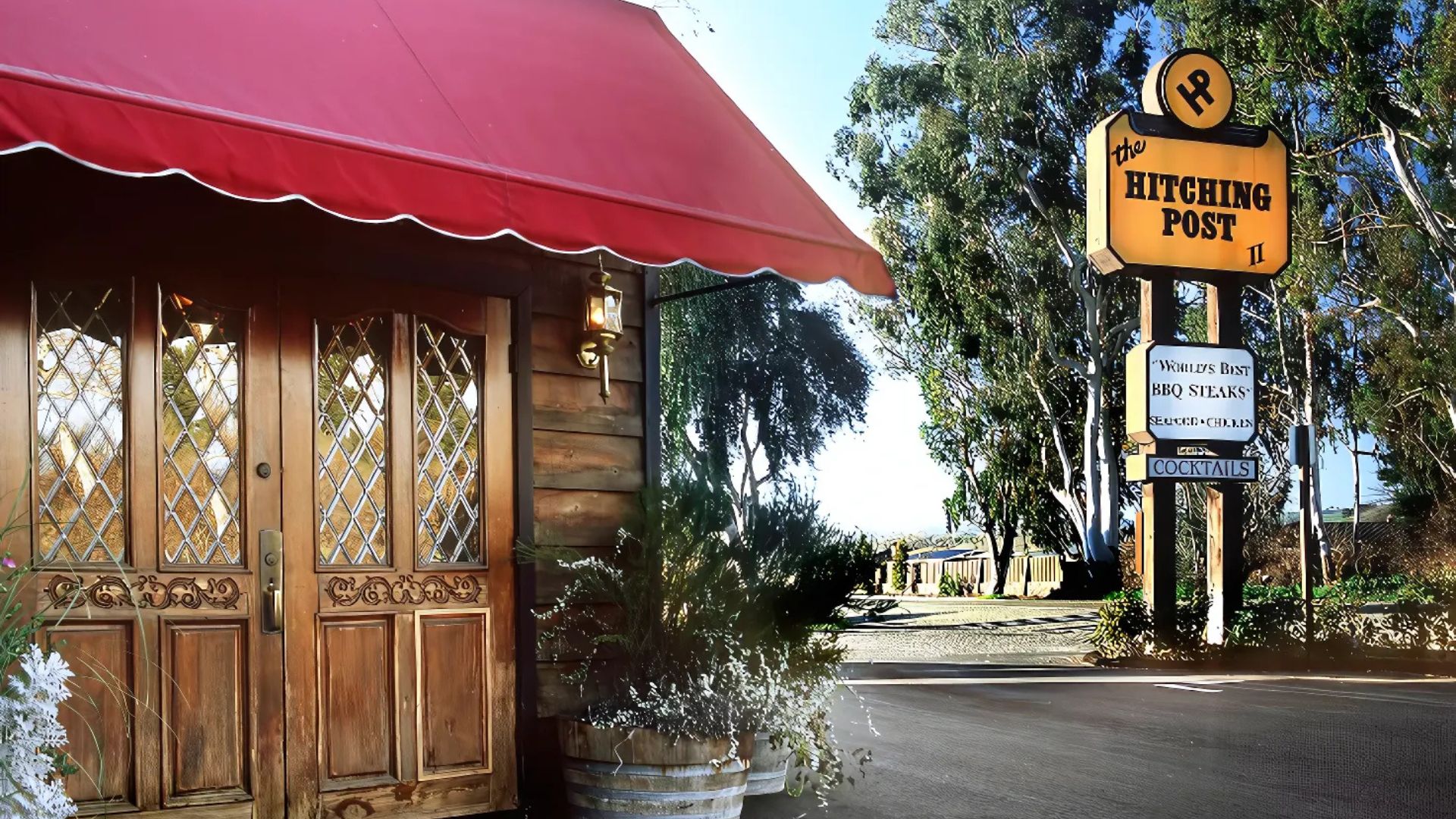 A well-appointed tasting room features wine bottles, some chilled in silver ice buckets, alongside rows of wine glasses and a wine rack, with a rustic wooden wall and a large trophy in the background.