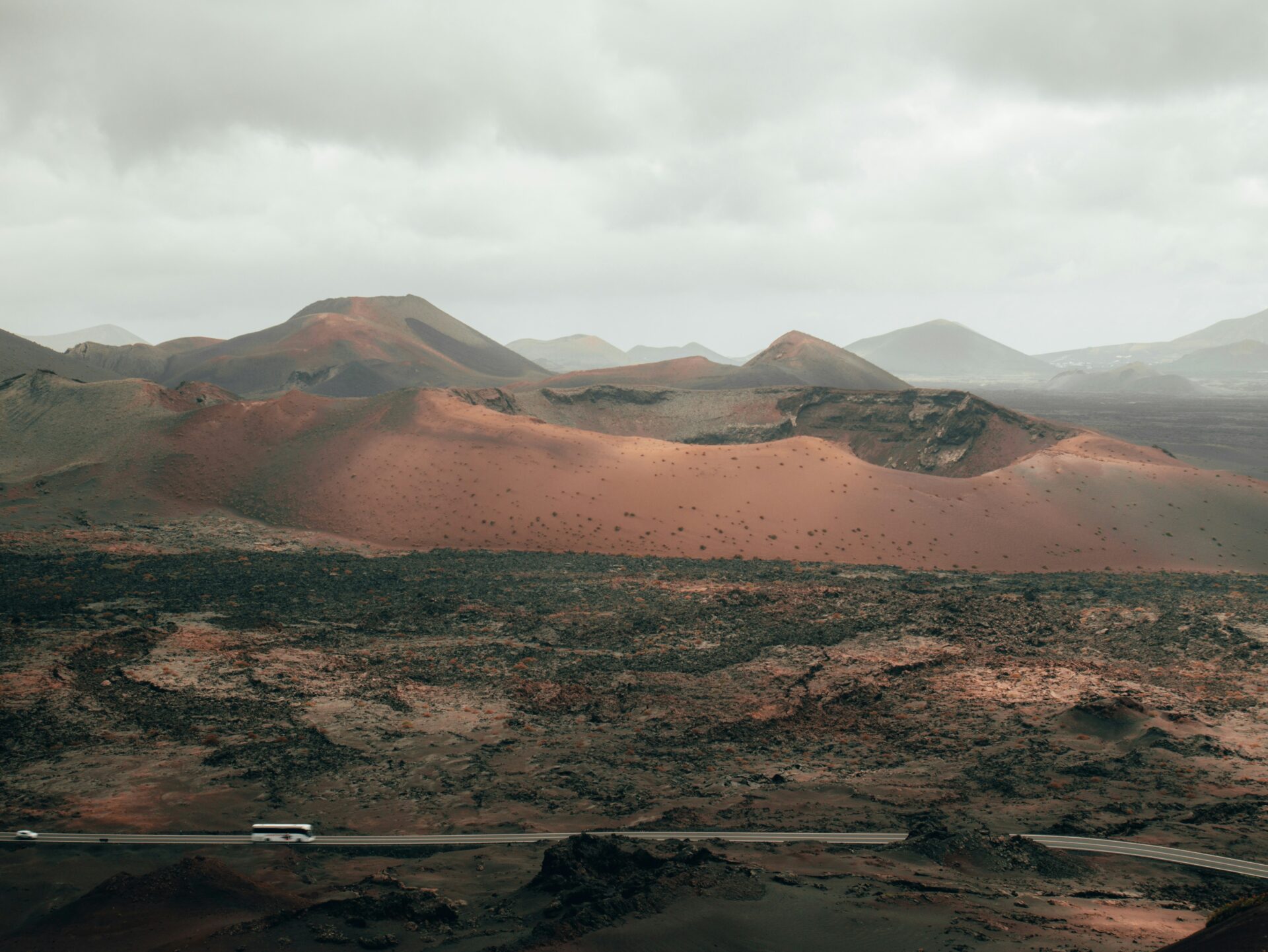 A tour bus driving along a narrow road through the volcanic landscape of Timanfaya National Park