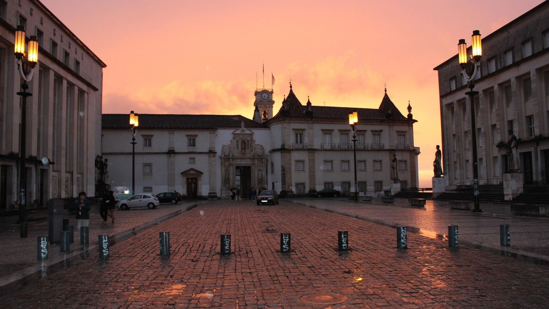 The image captures the historic University of Coimbra in Portugal at sunset, showcasing its iconic architecture and the charming cobblestone square, bathed in the warm glow of the evening sky. 