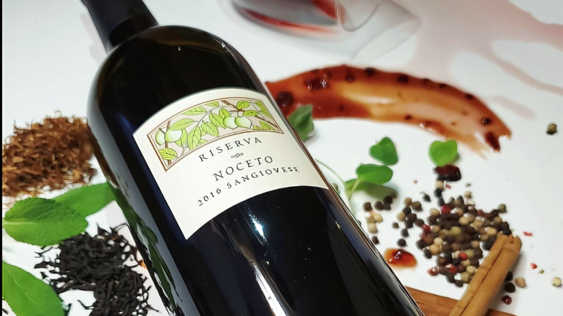 A close-up shot of a dark glass wine bottle, labeled "RISERVA NOCETO 2016 SANGIOVESE," resting on a white surface. Scattered around the bottle are various elements suggesting wine characteristics, including dried herbs, peppercorns, cinnamon sticks, and a smear of red liquid, possibly wine or a sauce, with a partially visible wine glass in the background.