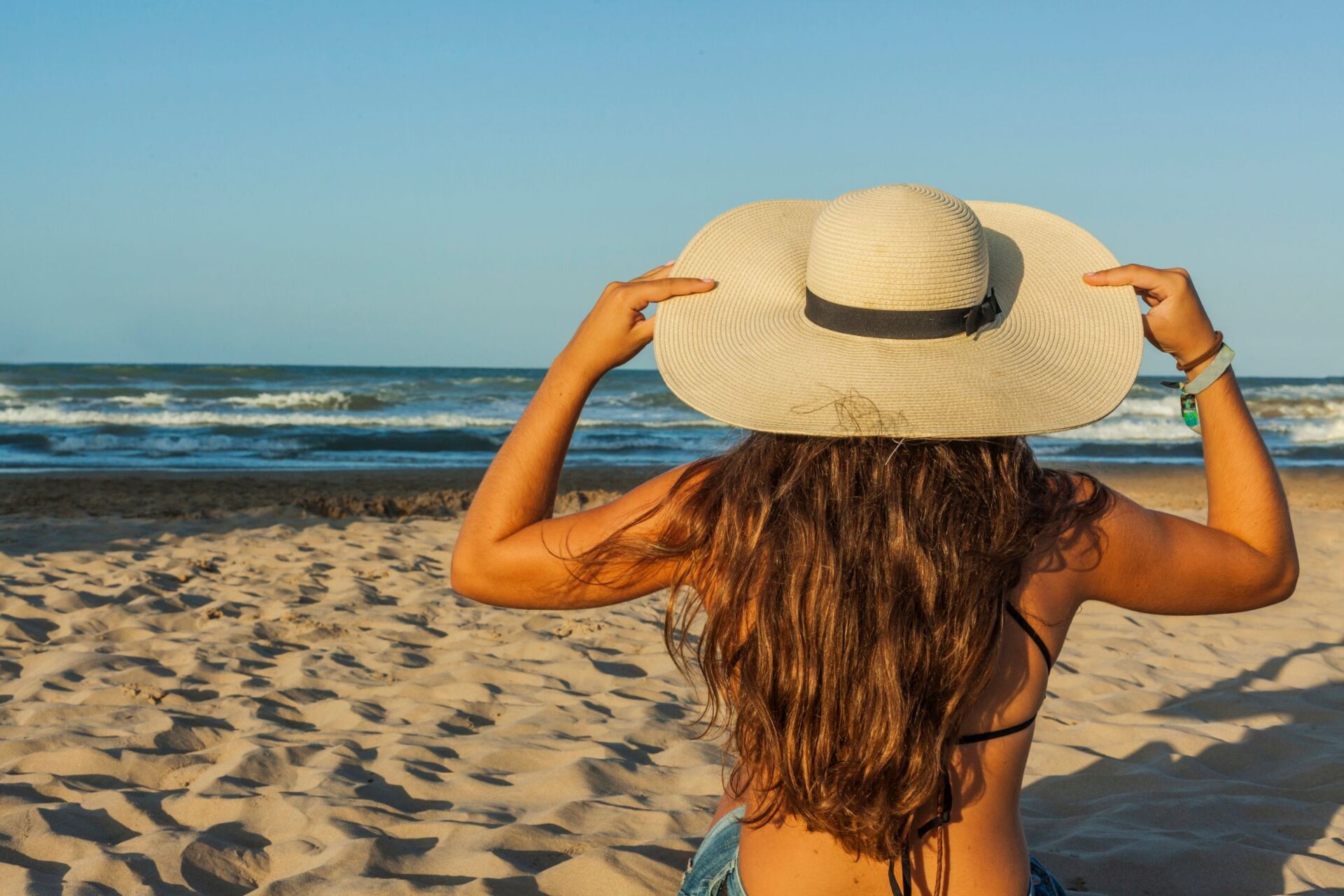 woman with sun hat sitting on the beach 