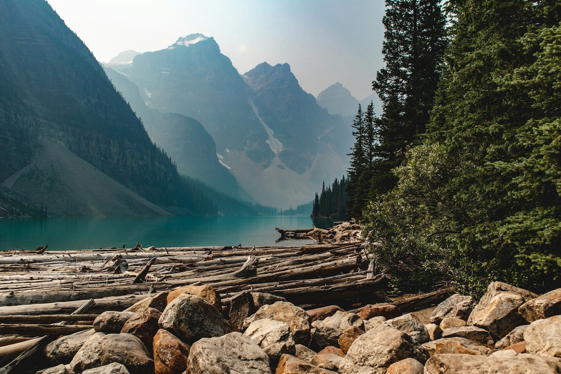 Scenic lake in Alberta surrounded by evergreen forests and mountains, with calm blue water reflecting the sky.