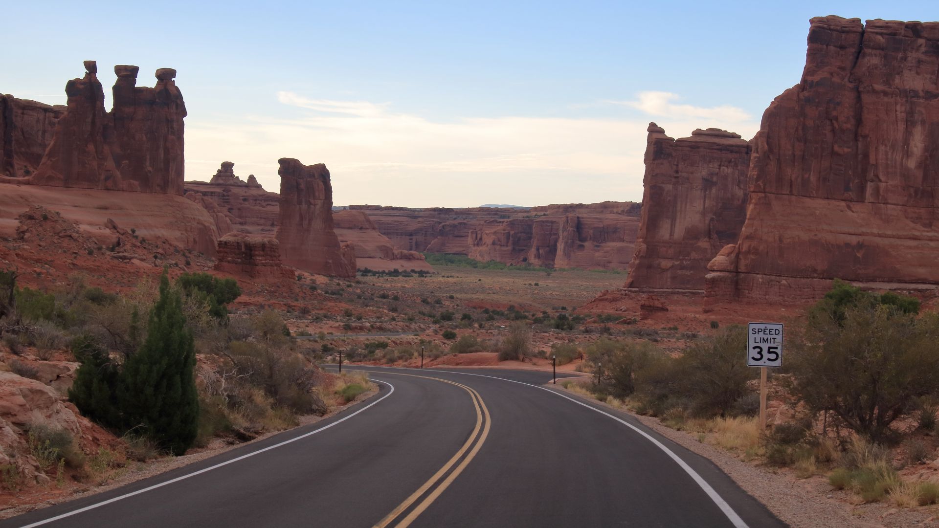 A winding paved road stretches into the distance, framed by towering red rock formations under a clear sky, with a "Speed Limit 35" sign visible on the right.