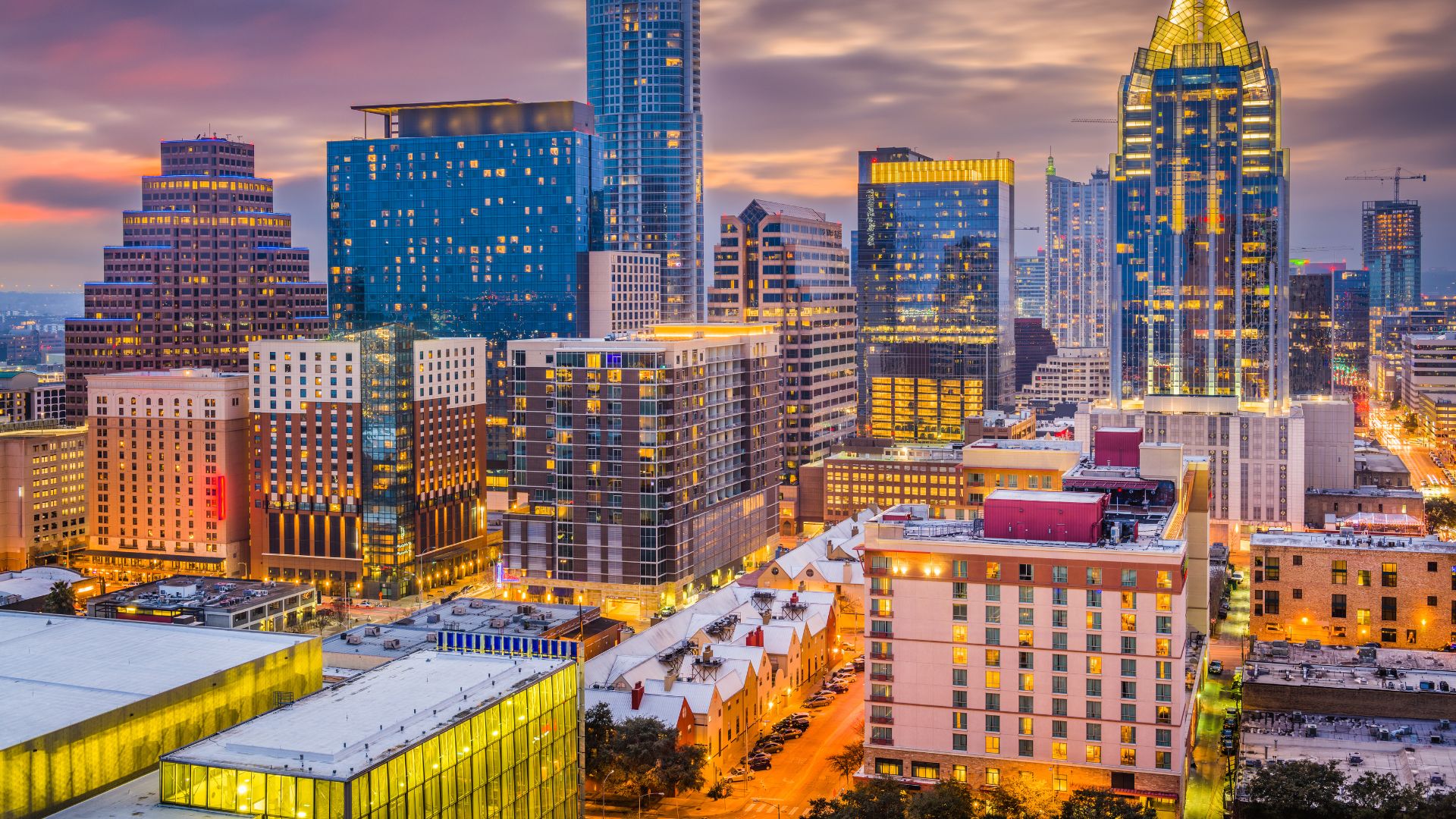 A vibrant cityscape at dusk featuring numerous high-rise buildings and illuminated streets, showcasing the Austin, Texas skyline.