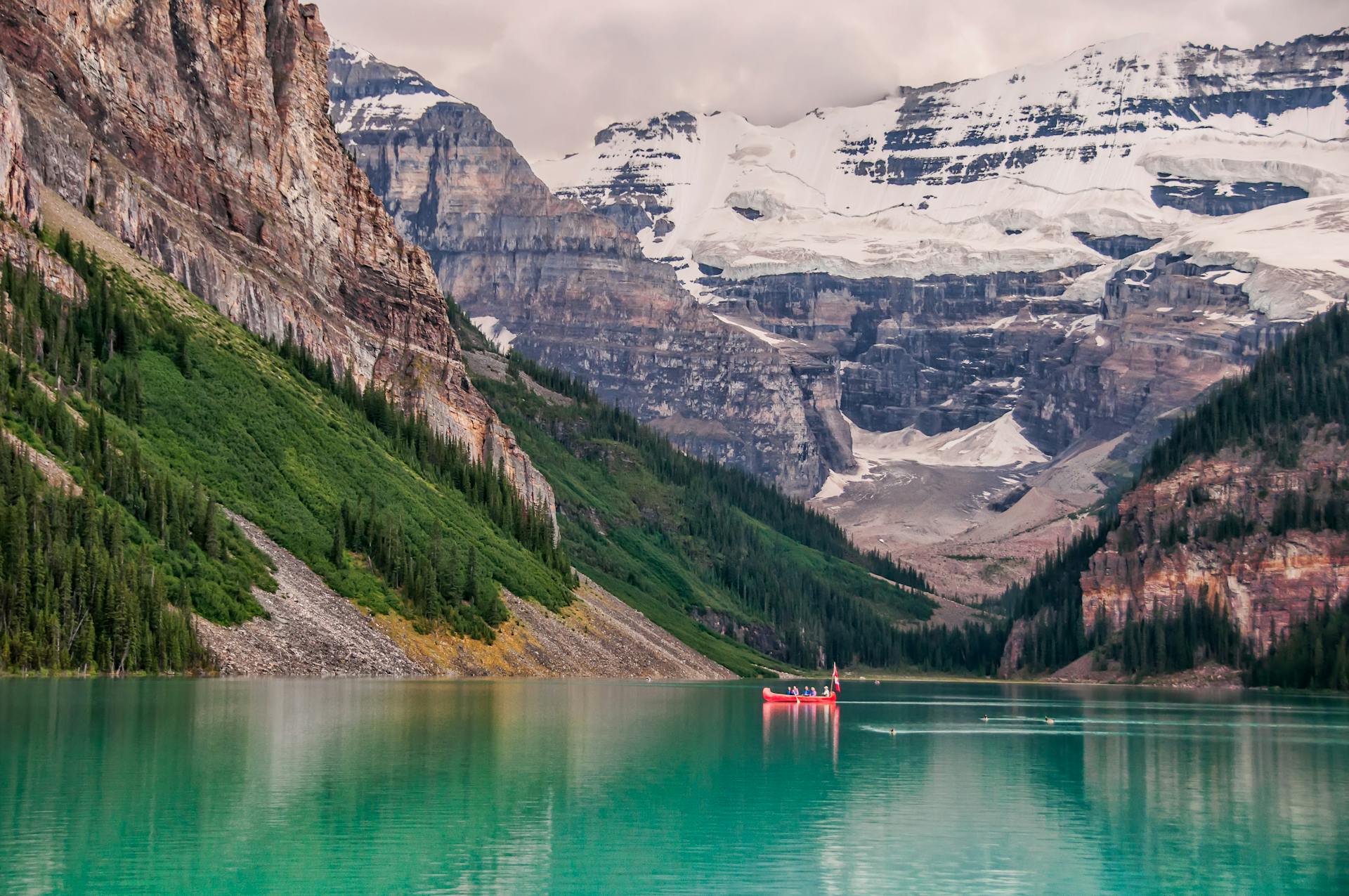 Crystal-clear lake in Banff National Park reflecting towering snow-capped mountains and lush pine forests under a bright blue sky.