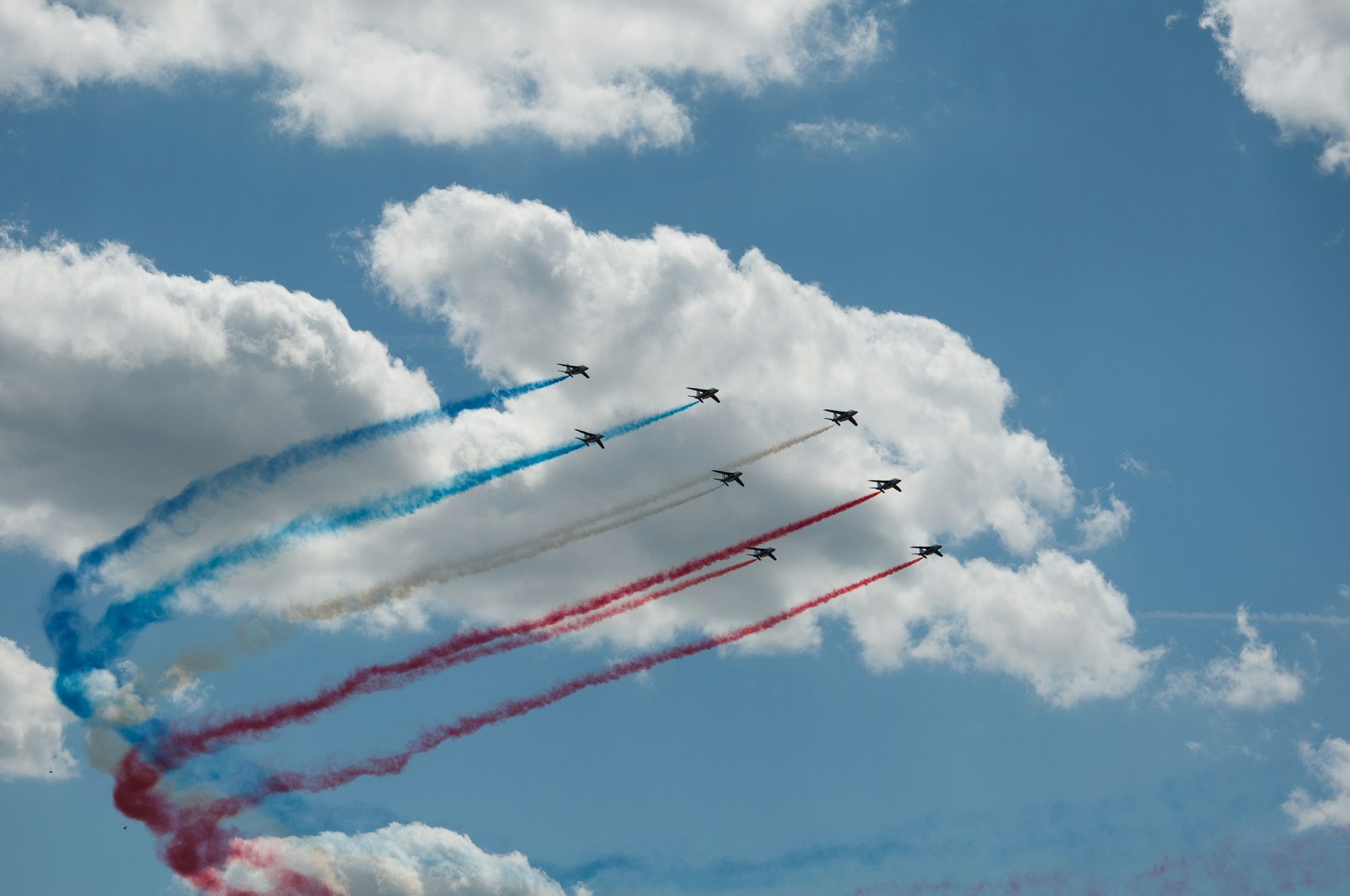 Jets soaring through the clear blue sky during the Bastille Day military parade, leaving trails of red, white, and blue smoke in their wake.