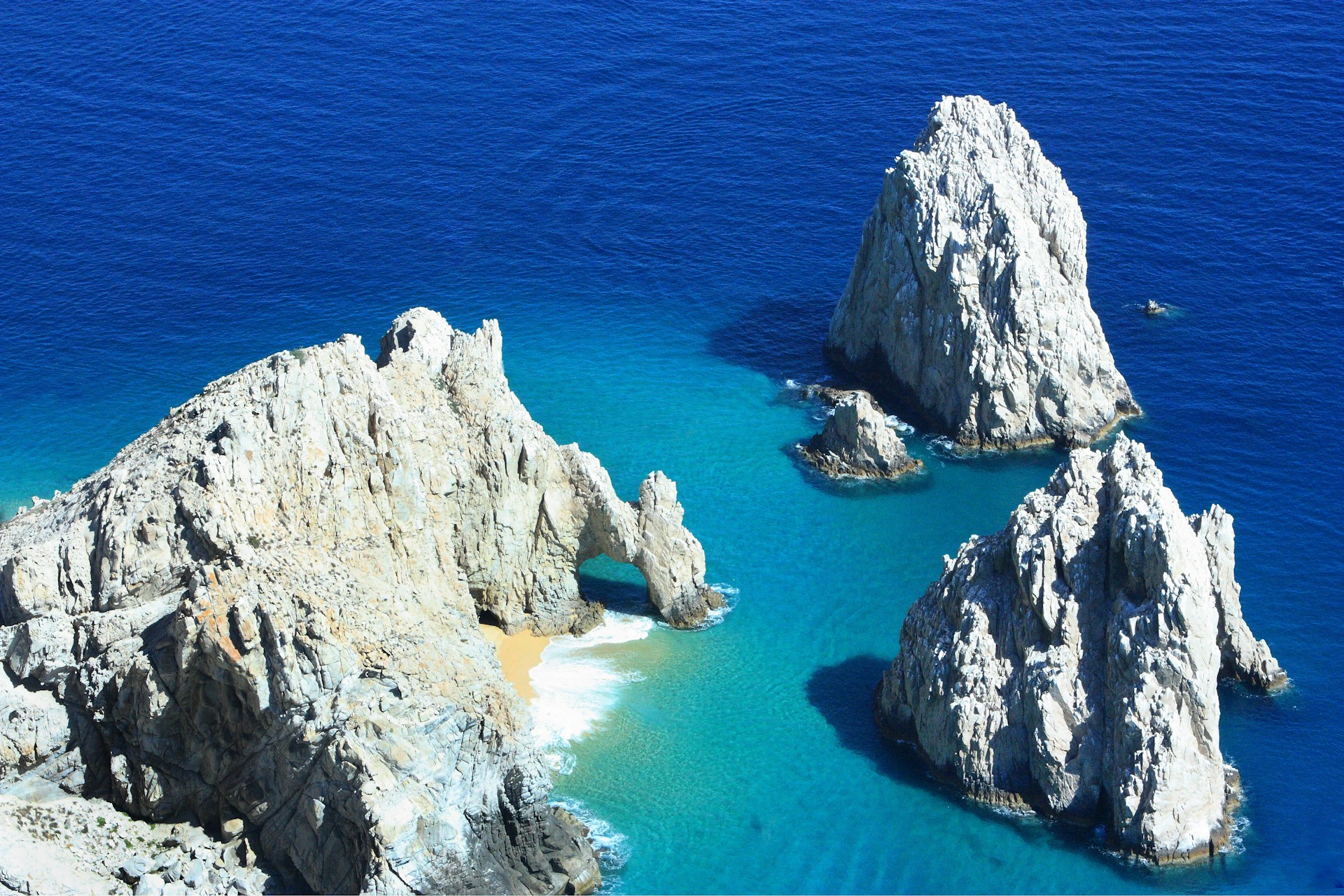 Golden sands stretching along the vibrant blue waters of Cabo beach, with rugged cliffs and iconic rock formations rising from the sea.