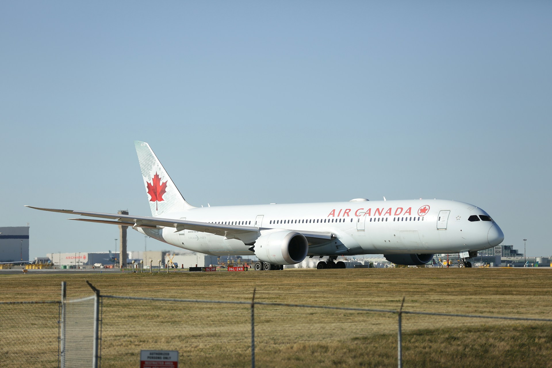 An Air Canada airplane on the runway, featuring the airline's signature red maple leaf logo on the tail and white fuselage, preparing for takeoff under a partly cloudy sky