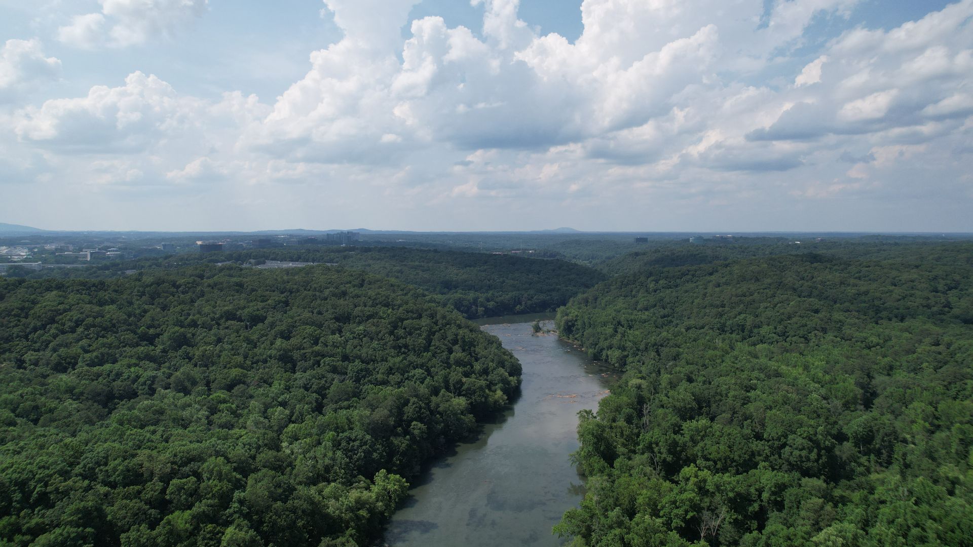A wide aerial view of the Chattahoochee River winding through a dense, green forest under a cloudy sky.