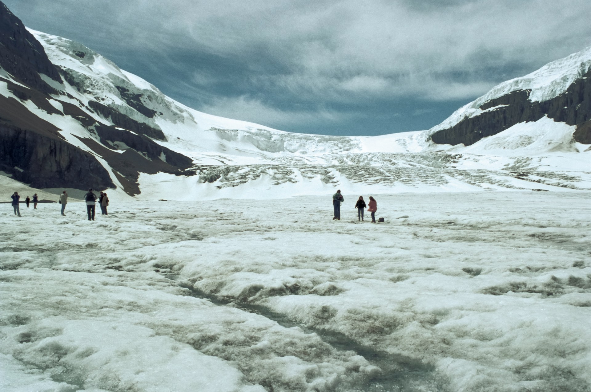 A receding Athabasca Glacier with exposed rocky terrain and signage marking its historical extent, highlighting the effects of climate change.
