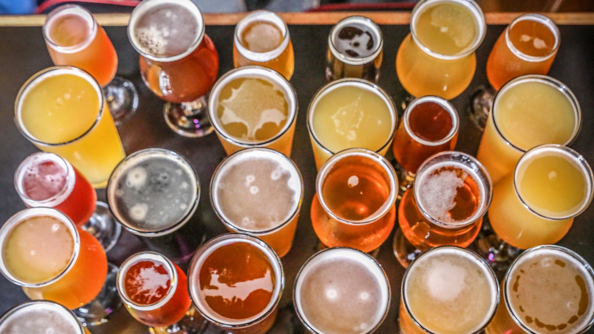 Overhead view of numerous glasses and pints filled with various types of craft beer, showcasing a range of colors and foam levels.