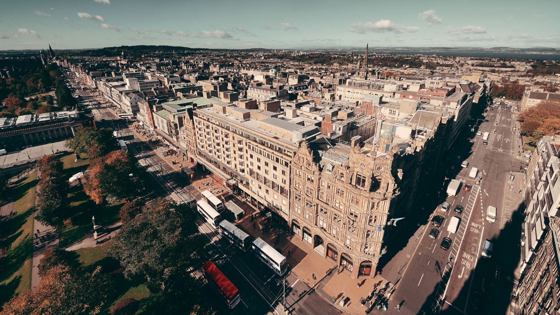 An aerial view of Edinburgh, Scotland, showcasing the city's historic architecture, including the prominent Scott Monument, and the surrounding urban landscape with streets and green spaces.