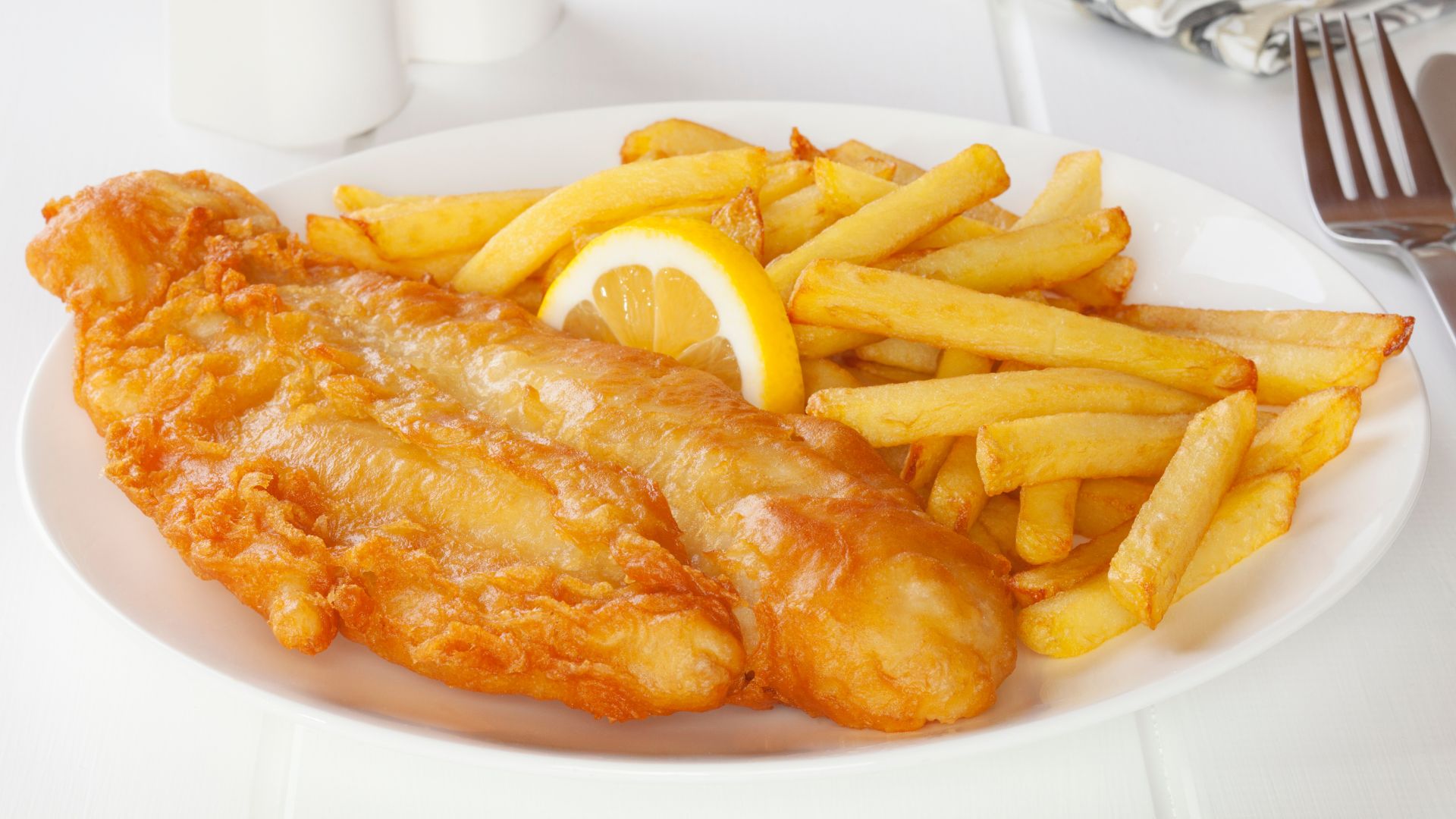 A plate of golden-brown battered fish fillets and a generous serving of crispy french fries, garnished with a lemon wedge.