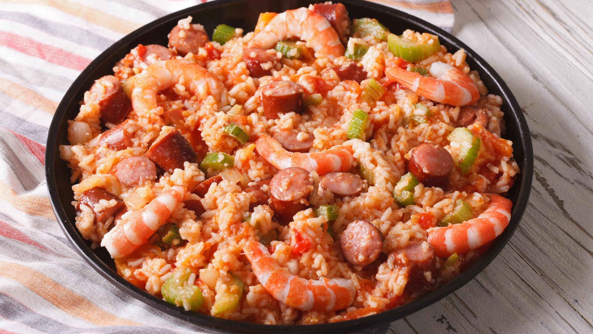 A close-up of a bowl of Jambalaya, a Creole rice dish, featuring shrimp, sliced sausage, rice, and green vegetables like okra or bell peppers. 