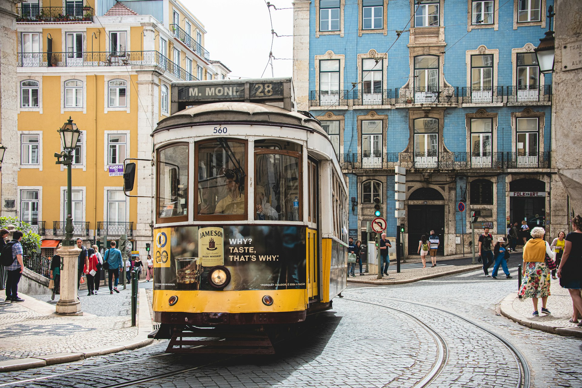 Iconic yellow tram in Lisbon traveling up a steep cobblestone street lined with historic buildings.