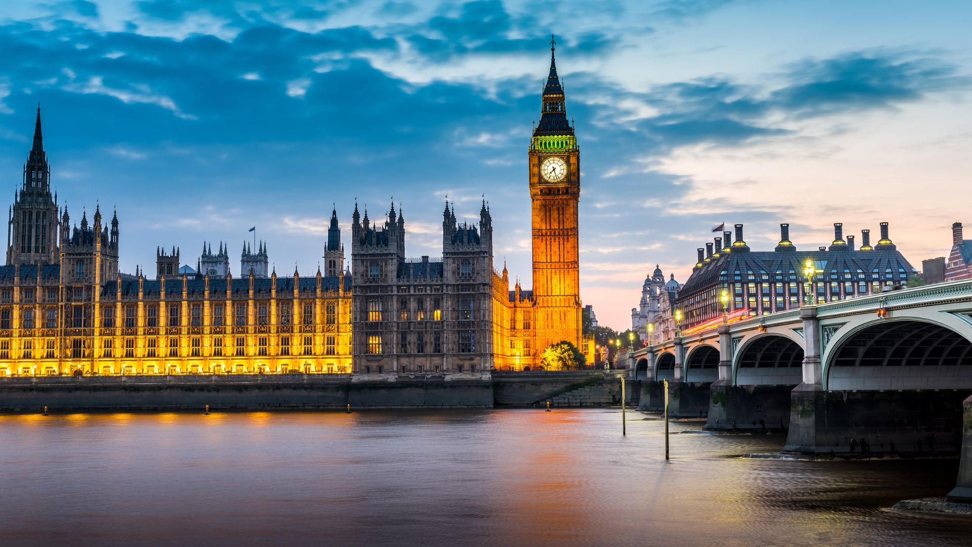An evening cityscape of the Houses of Parliament and the Elizabeth Tower (Big Ben) illuminated along the River Thames in London, United Kingdom.
