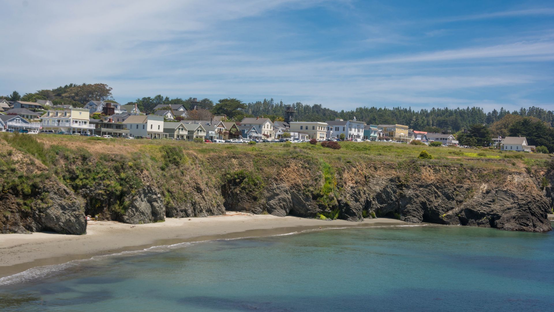 A scenic view of the coastal town of Mendocino, California, situated on a bluff overlooking a sandy beach and the Pacific Ocean under a clear blue sky.