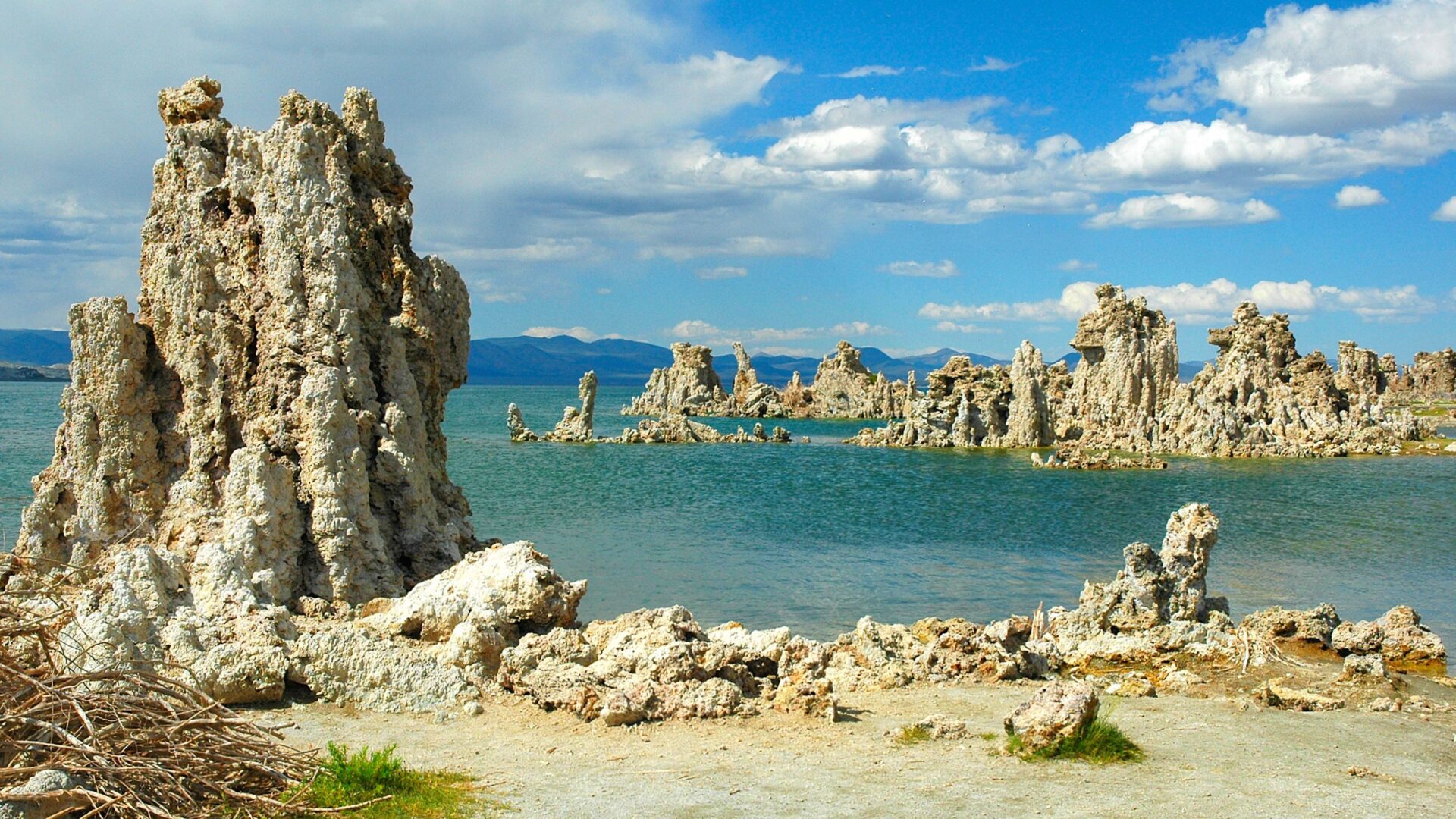 Tufa formations rising from the alkaline waters of Mono Lake in California under a blue sky with scattered clouds.