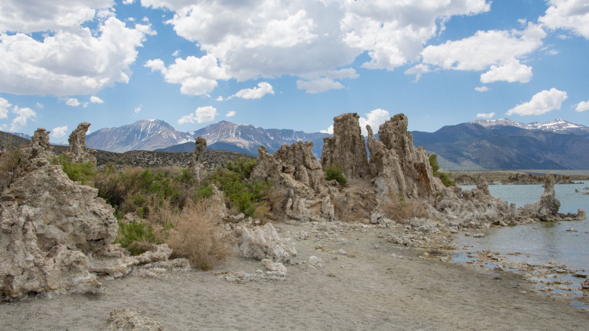 A panoramic view of Mono Lake's South Tufa Area in California, featuring striking tufa formations along the shoreline with mountains and a cloudy sky in the background.