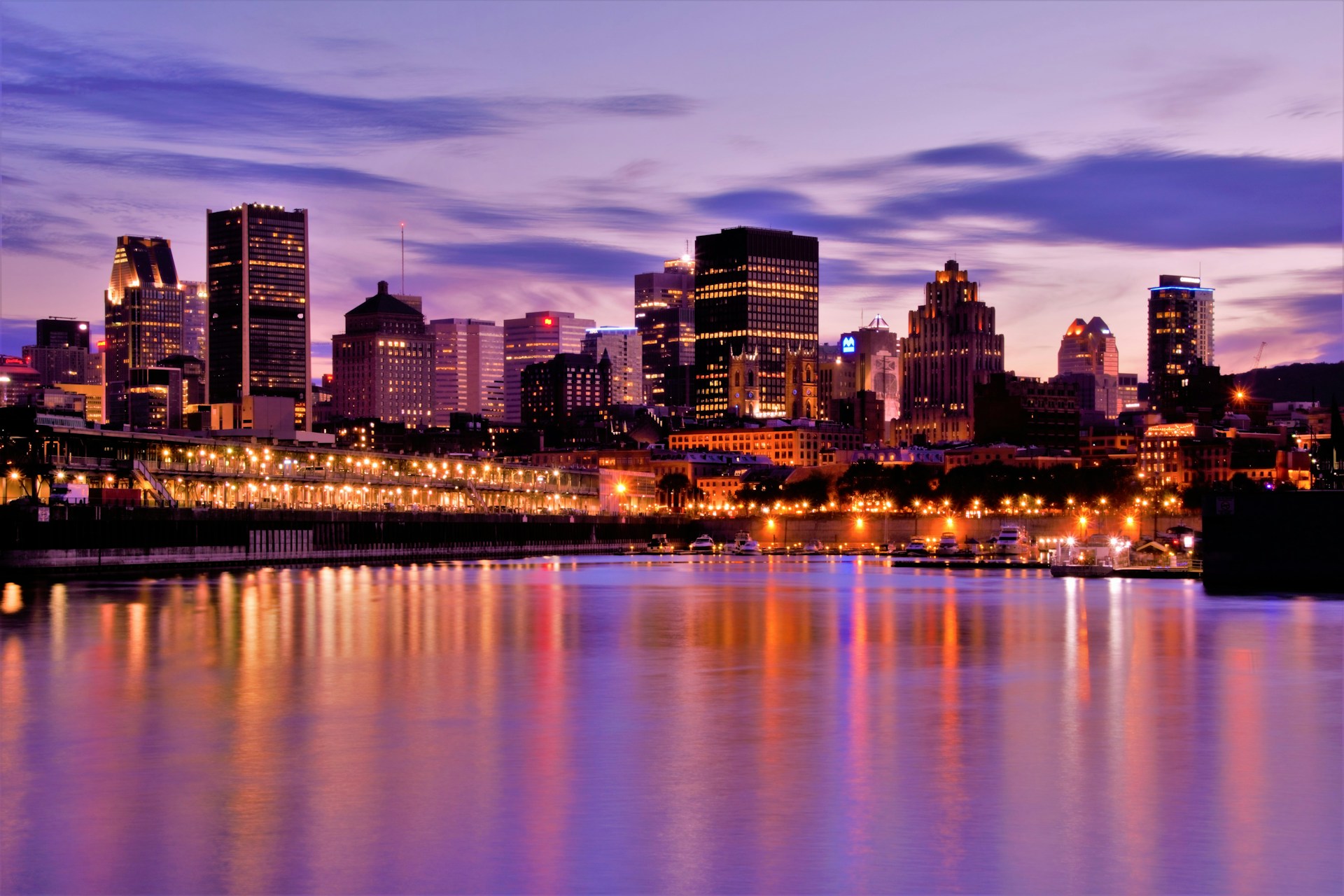 Montreal skyline at night with city lights glowing from high-rise buildings and Mount Royal silhouetted in the background.