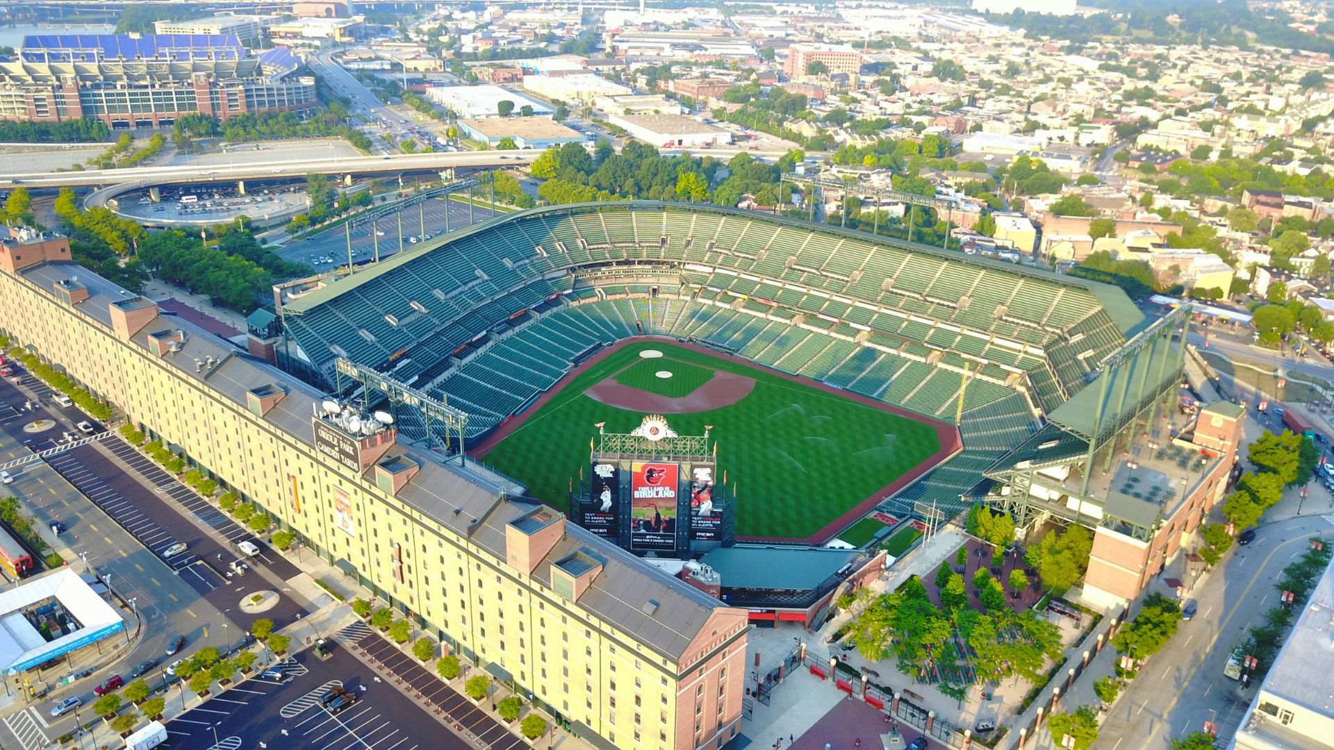 An aerial view of Oriole Park at Camden Yards, a baseball stadium in downtown Baltimore, Maryland, surrounded by city buildings and infrastructure under a clear sky.