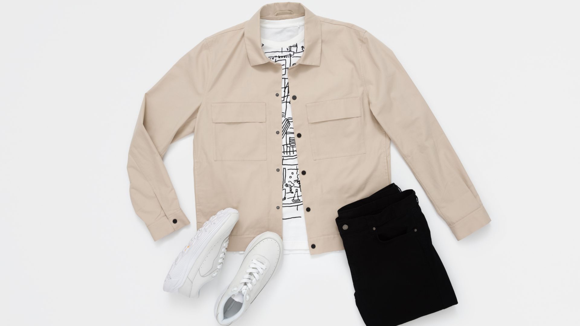 A flat lay featuring men's casual wear, including a beige overshirt, a white graphic t-shirt, black jeans, and white sneakers, arranged neatly on a light background.