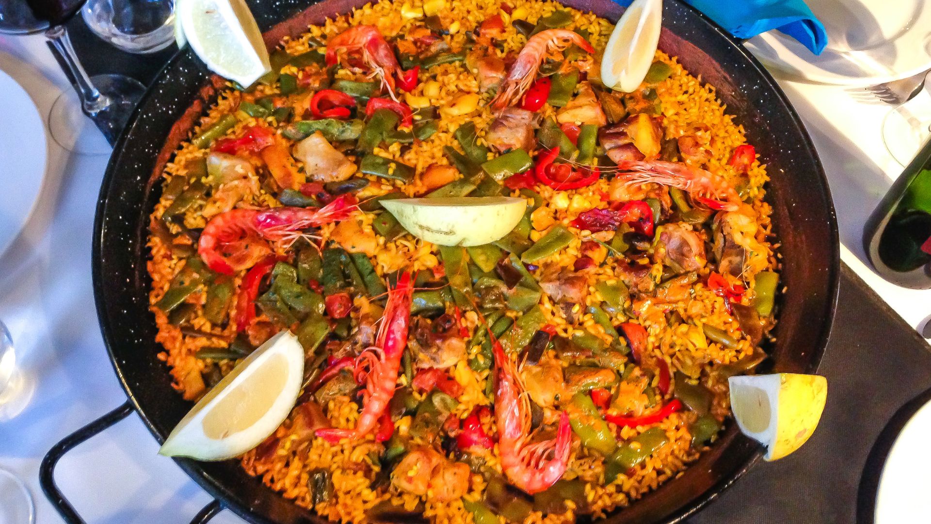 A large pan filled with vibrant seafood paella, garnished with lemon wedges.